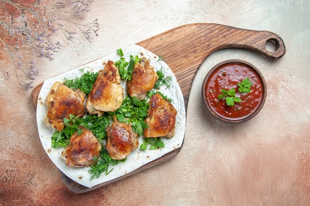 Top close-up view chicken pieces of chicken with herbs on lavash on the board bowl of sauce