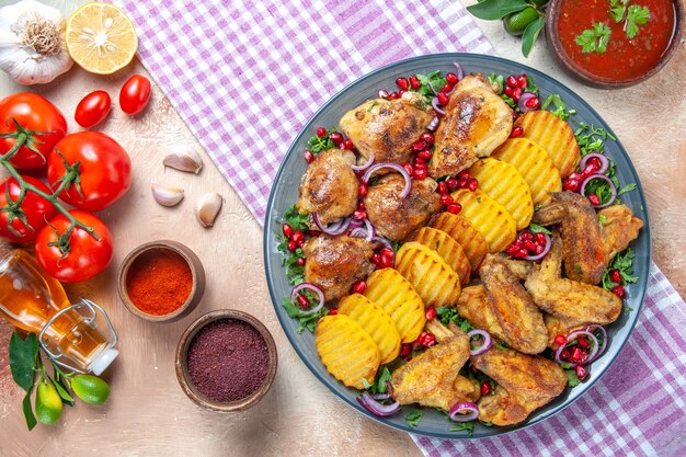 Top close-up view chicken plate of chicken wings potatoes lemon oil garlic tomatoes spices