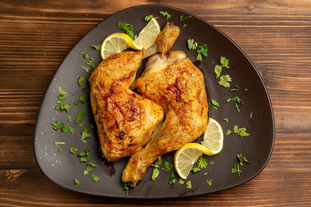 테이블 중앙에 있는 갈색 접시에 허브와 레몬을 넣은 허브 치킨 다리가 있는 클로즈업 보기 치킨