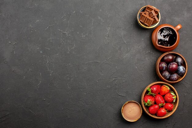 어두운 테이블의 오른쪽에 있는 딸기 초콜릿 소스와 딸기의 상단 클로즈업 보기 초콜릿 베리 갈색 그릇