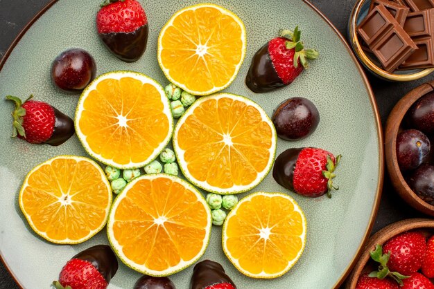 Top close-up view choped orange and chocolate white plate of chopped orange chocolate and candies next to bowls of chocolate and berries on the dark background