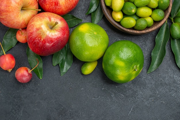 Top close-up view citrus fruits apples cherries mandarins bowl of citrus fruits with leaves