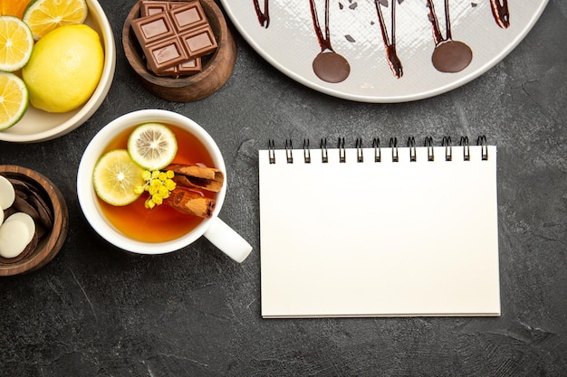 Vista ravvicinata dall'alto agrumi ciotole di cioccolato di agrumi e cioccolato accanto al quaderno bianco e una tazza di tè al limone