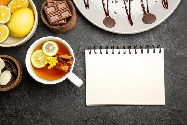 흰색 공책 옆에 있는 감귤류 과일 초콜릿 그릇과 레몬 차 한 잔