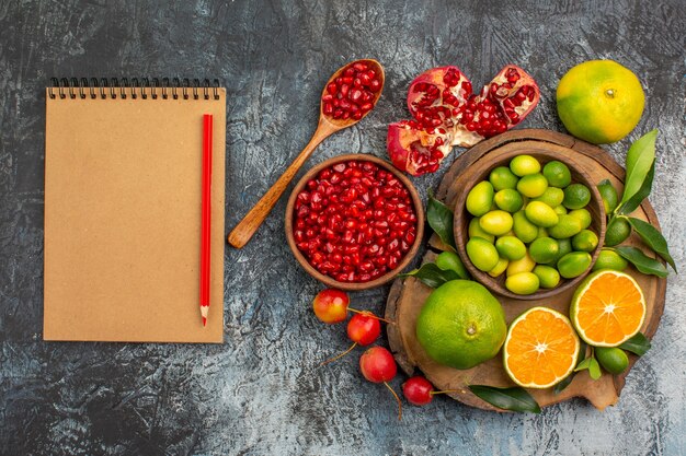 Top close-up view citrus fruits pomegranate seeds spoon citrus fruits on the board notebook pencil