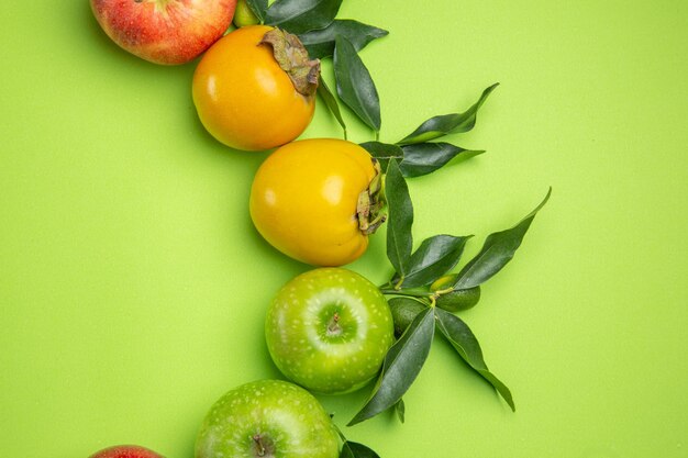Top close-up view colorful fruits green apples persimmons with leaves on the table