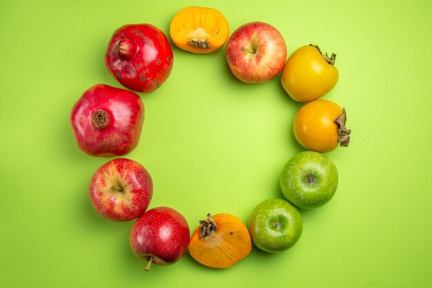 Top close-up view colorful fruits persimmons apples pomegranate on the green table