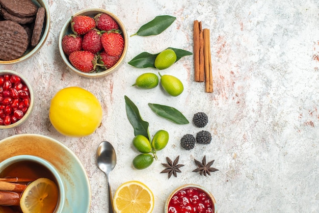 Free photo top close-up view cookies and berries cinnamon the appetizing cookies strawberries lemon spoon a cup of tea citrus fruits on the table