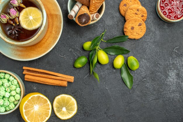 Top close-up view a cup of tea cookies a cup of tea candies jam lemon cinnamon citrus fruits