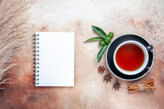 Top close-up view a cup of tea a cup of tea cinnamon sticks citrus fruits white notebook