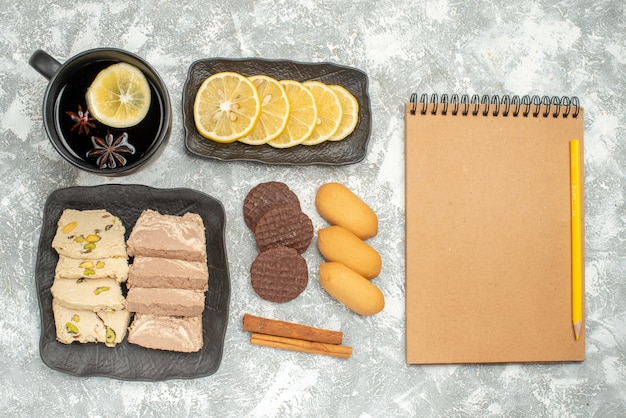 Top close-up view a cup of tea a cup of tea lemon sweets on the plate pencil notebook