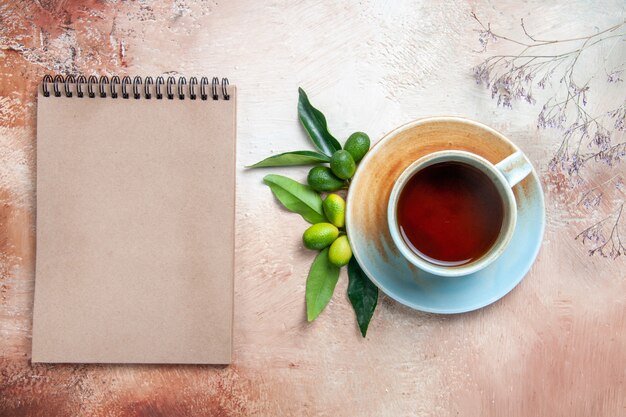 Top close-up view a cup of tea a cup of tea on the saucer citrus fruits cream notebook