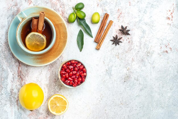 Top close-up view a cup of tea a cup of tea with lemon and cinnamon on the saucer with citrus fruits pomegranate star anise and cinnamon sticks on the table