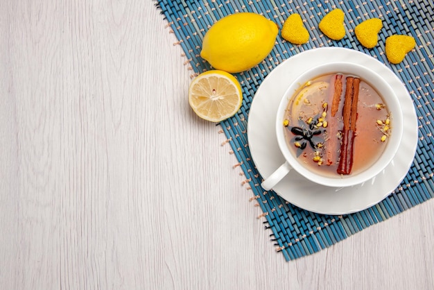 Top close-up view a cup of tea with cinnamon a cup of tea with lemon and cinnamon sticks lemon sweets on the blue-white tablecloth