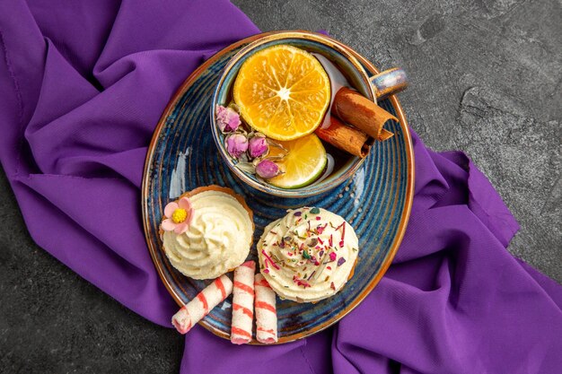 Вид сверху крупным планом чашка чая с лимонными аппетитными кексами с чашкой чая на фиолетовой скатерти на столе