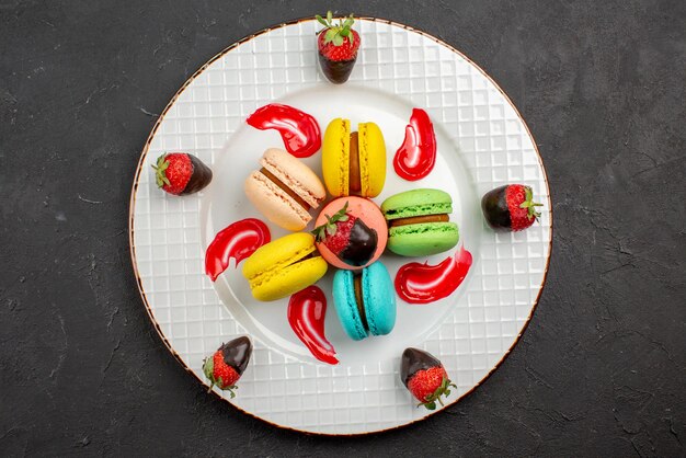 Top close-up view dessert appetizing French macaroon with chocolate-covered strawberries on the dark table