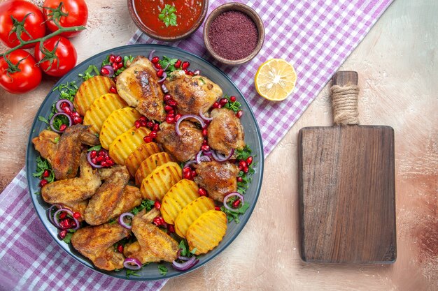 Top close-up view dish chicken wings potatoes tomatoes sauce spices the cutting board