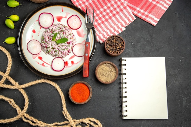 Top close-up view a dish dish of redish fork bowls of spices the checkered tablecloth notebook