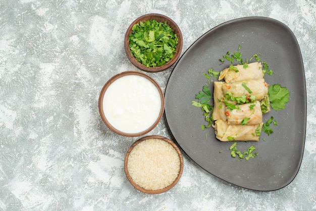 Free photo top close-up view dish with herbs dish of stuffed cabbage next to bowls of herbs sour cream rice on grey surface