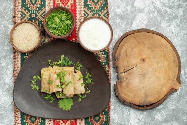 Top close-up view dish with herbs grey plate of stuffed cabbage rice herbs sour cream on colored tablecloth with patterns on the left side of the table next to cutting board