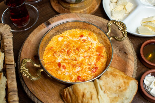 A top close up view eggs cooked with red tomatoes inside metallic pan along with hot tea and bread slices