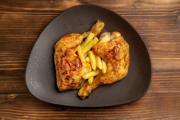 Top close-up view fast food brown plate of appetizing french fries and chicken legs on the wooden table