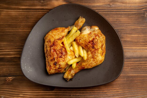 Top close-up view fast food brown plate of appetizing french fries and chicken legs on the wooden table