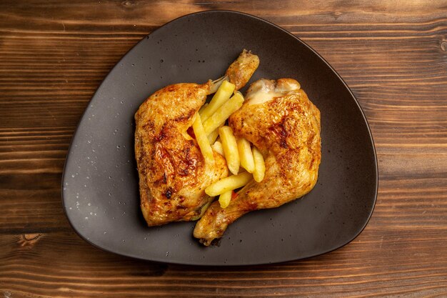 Сверху крупным планом коричневая тарелка быстрого питания с аппетитным картофелем фри и куриными ножками на деревянном столе