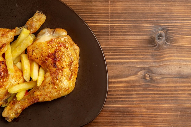 Top close-up view fast food chicken french fries on the plate on the left side of the wooden table