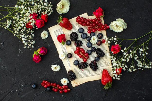 A top close up view fresh berries colored different red berries and blackberries on the paper and dark floor