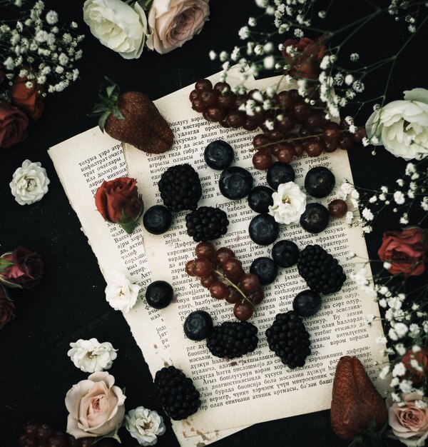 A top close up view fresh fruits such as blueberries and blackberries along with others on the paper and dark floor
