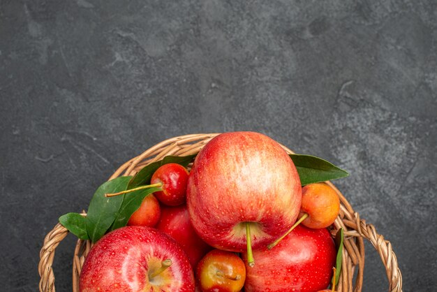 暗いテーブルの上のバスケットの上のクローズアップビューフルーツリンゴとサクランボ