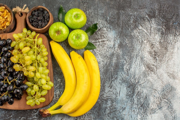 Vista ravvicinata dall'alto frutta banane ciotole di frutta secca mele con foglie e uva sul tabellone