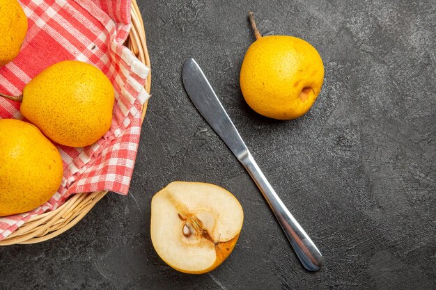 Top close-up view fruits in the basket appetizing pears on the checkered tablecloth in the basket next to the knife pear and half a pear on the dark table