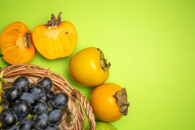 Top close-up view fruits basket of black grapes the appetizing persimmons on the green background