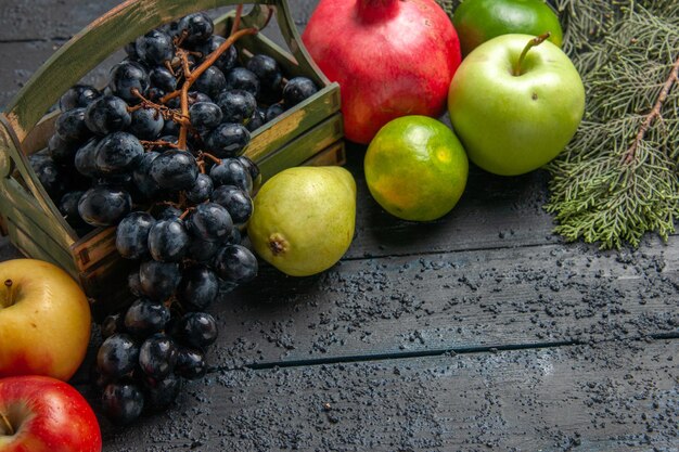 上のクローズアップビューフルーツブドウの木箱のリンゴザクロ梨ライム暗いテーブルのトウヒの枝の横にある