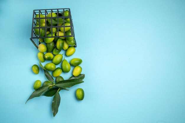 Top close-up view fruits green citrus fruits with leaves in the grey basket on the blue table