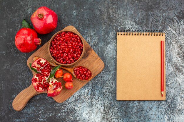 Top close-up view fruits notebook pencil the board with pomegranate spoon cherries