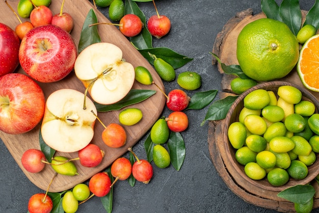 Top close-up view fruits red apples on the board cherries and citrus fruits in bowl