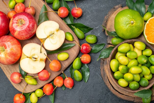 Top close-up view fruits red apples on the board cherries and citrus fruits in bowl