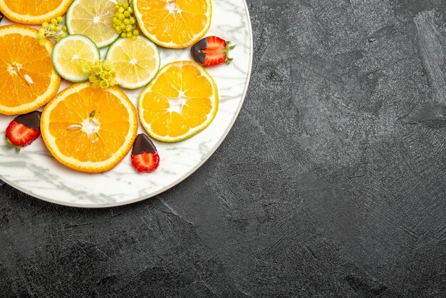 테이블 왼쪽에 있는 흰색 접시에 초콜릿으로 덮인 딸기 슬라이스 레몬 오렌지