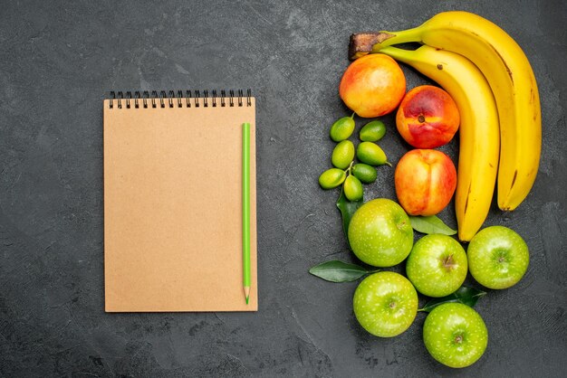 Top close-up view fruits on the table notebook pencil next to the apples bananas and nectarines