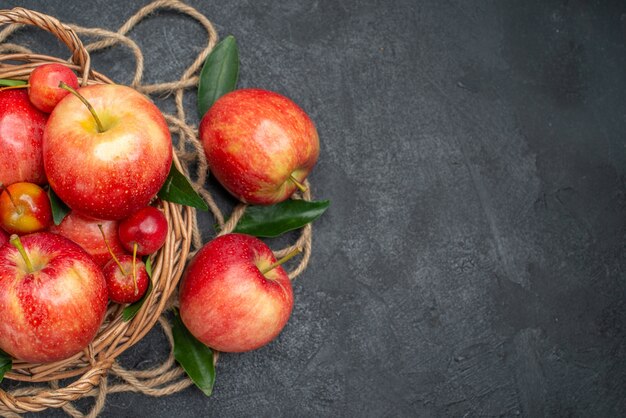 Top close-up view fruits wooden basket of apples and cherries with leaves