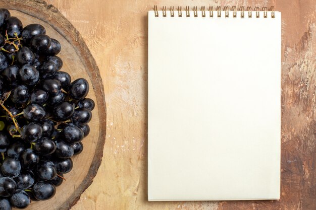 Top close-up view grapes bunches of black grapes on the wooden cutting board white notebook