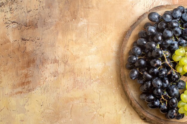 top close-up view grapes wooden board with green and black grapes on the cream table