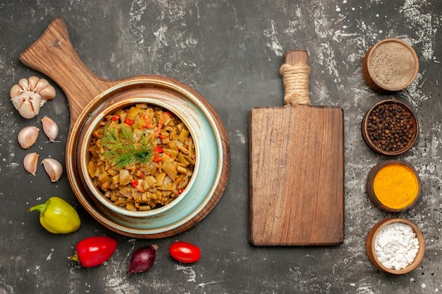 Foto gratuita vista ravvicinata dall'alto fagiolini taccuino bianco piatto dei fagiolini con pomodori sul tagliere peperoni cipolla aglio tagliere e ciotole di spezie sul tavolo scuro