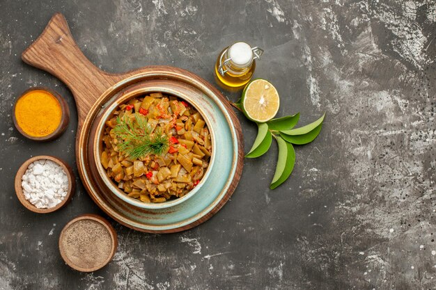 Free photo top close-up view green beans with tomatoes tomatoes and green beans in the plate and three kinds of spices next to the bottle of oil lemon and leaves