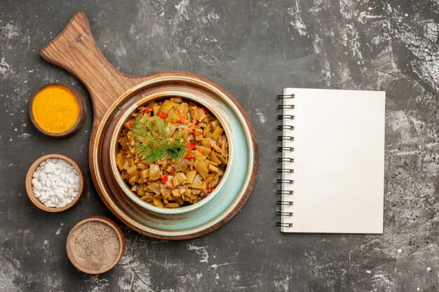 Top close-up view green beans with tomatoes white notebook next to the board with plate of green beans and three spices