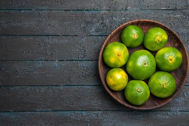 Top close-up view limes in bowl green limes in wooden bowl on the grey background