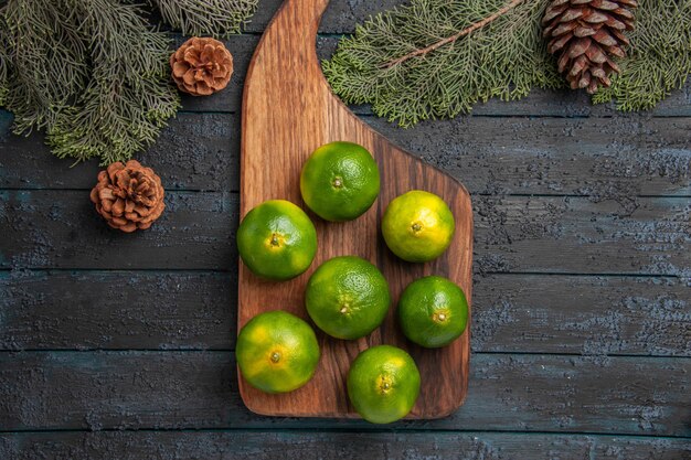 Top close-up view limes and branches limes on the kitchen board next to the tree branches and cones